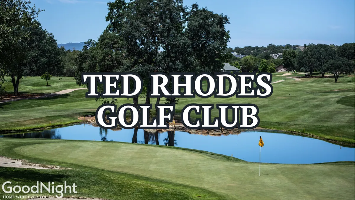 An inviting view of a golf course with manicured grass, a water feature, trees, and a flag on the green, highlighting the recreational opportunities at Ted Rhodes Golf Club.