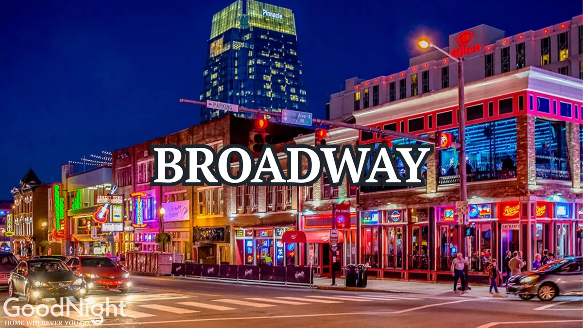 This exterior street scene captures a busy Nashville night, with neon signs illuminating the street, people strolling past, and cars moving through the lively cityscape. The vibrant atmosphere conveys the heart of Nashville’s nightlife.