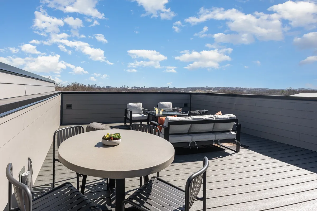 A serene rooftop seating area is featured in this image, with a round table surrounded by chairs and the Nashville skyline rising in the background. The scene suggests an ideal spot for entertaining or unwinding, especially during sunset or evening hours.