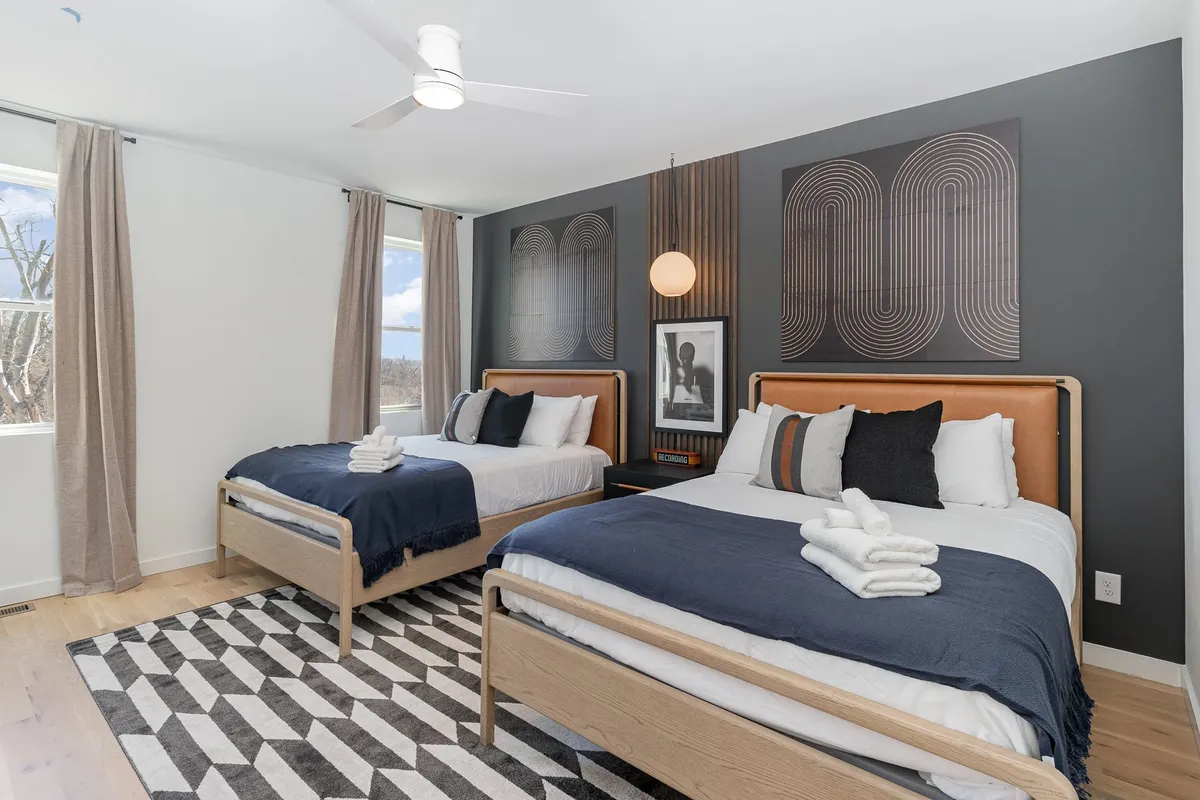The second bedroom is depicted with two stylish beds, modern geometric artwork above, and a contemporary round pendant light. The arrangement offers both comfort and a visually appealing environment.