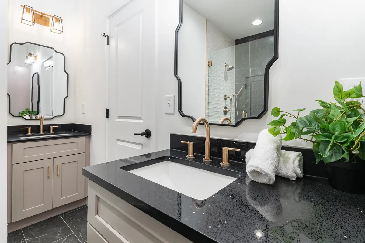 A sophisticated bathroom setup with a black granite countertop, elegant fixtures, a mirrored vanity, fresh towels, and a touch of greenery. The scene radiates comfort and readiness for guests' routines.