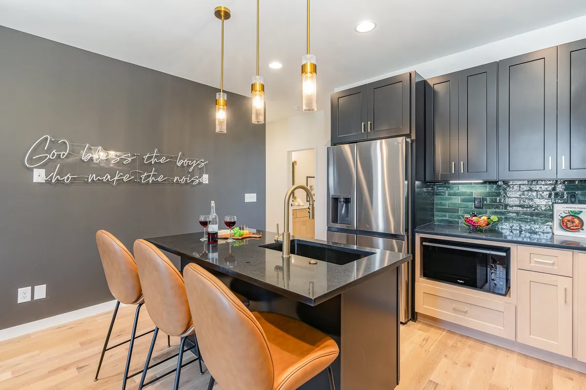 A modern, welcoming kitchen featuring a central island with bar stools, sleek appliances, and a stylish neon sign. The space is open and perfect for prepping meals or gathering before heading out, with everything needed for convenience at your fingertips.