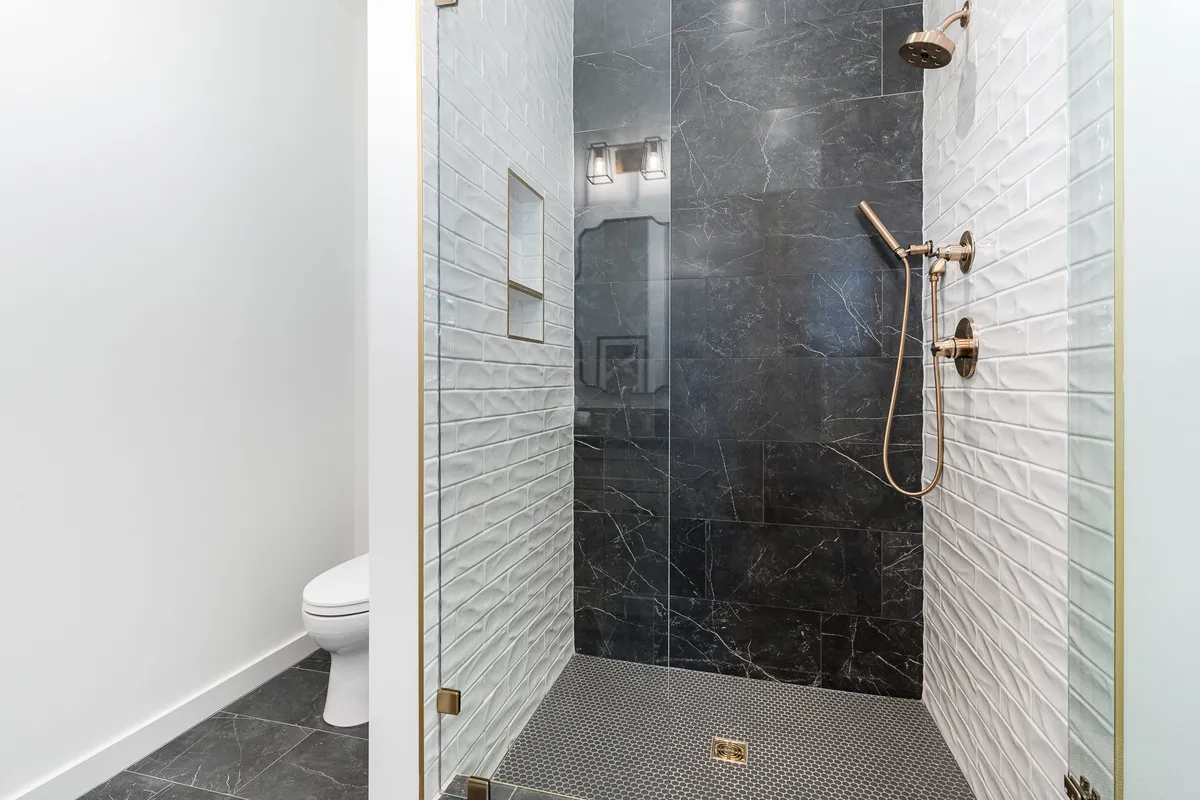 A serene bathroom scene showcases a modern shower enclosure with striking tile patterns and gold fixtures, radiating spa-like luxury. The space is bright, clean, and inviting—perfect for unwinding.