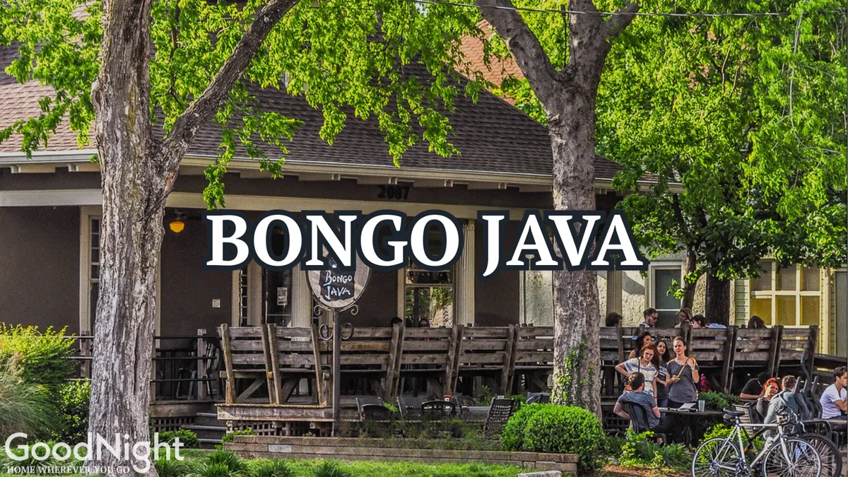 A sunny exterior view of Bongo Java coffeehouse with its distinctive signage, outdoor seating, and lush green trees. People gather outside, chatting and enjoying coffee in a relaxed, friendly atmosphere.