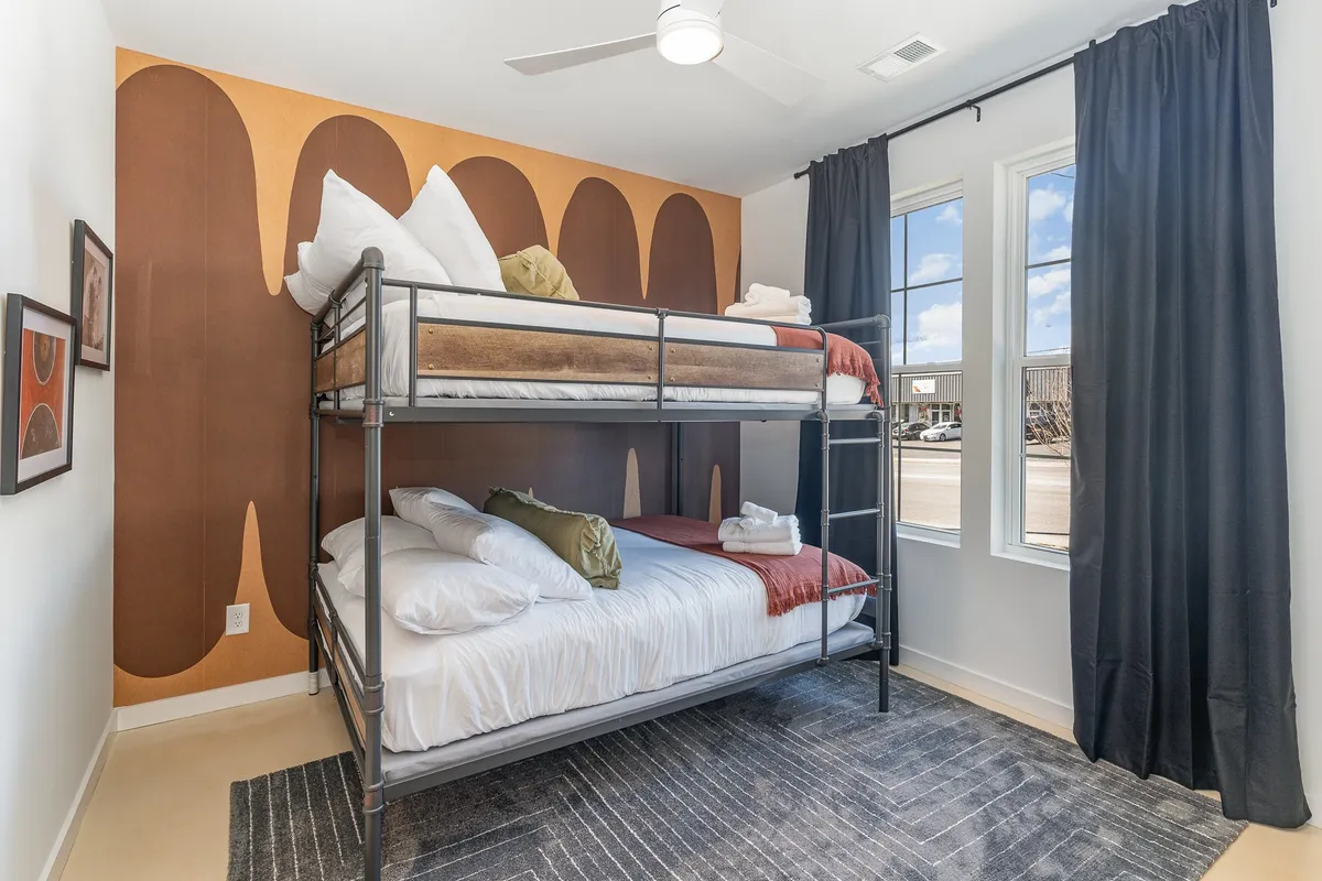 A cheerful bedroom with a sturdy bunk bed, colorful wall art, and sunlit windows. The layout is clearly family-friendly, with ample space for extra sleeping arrangements.